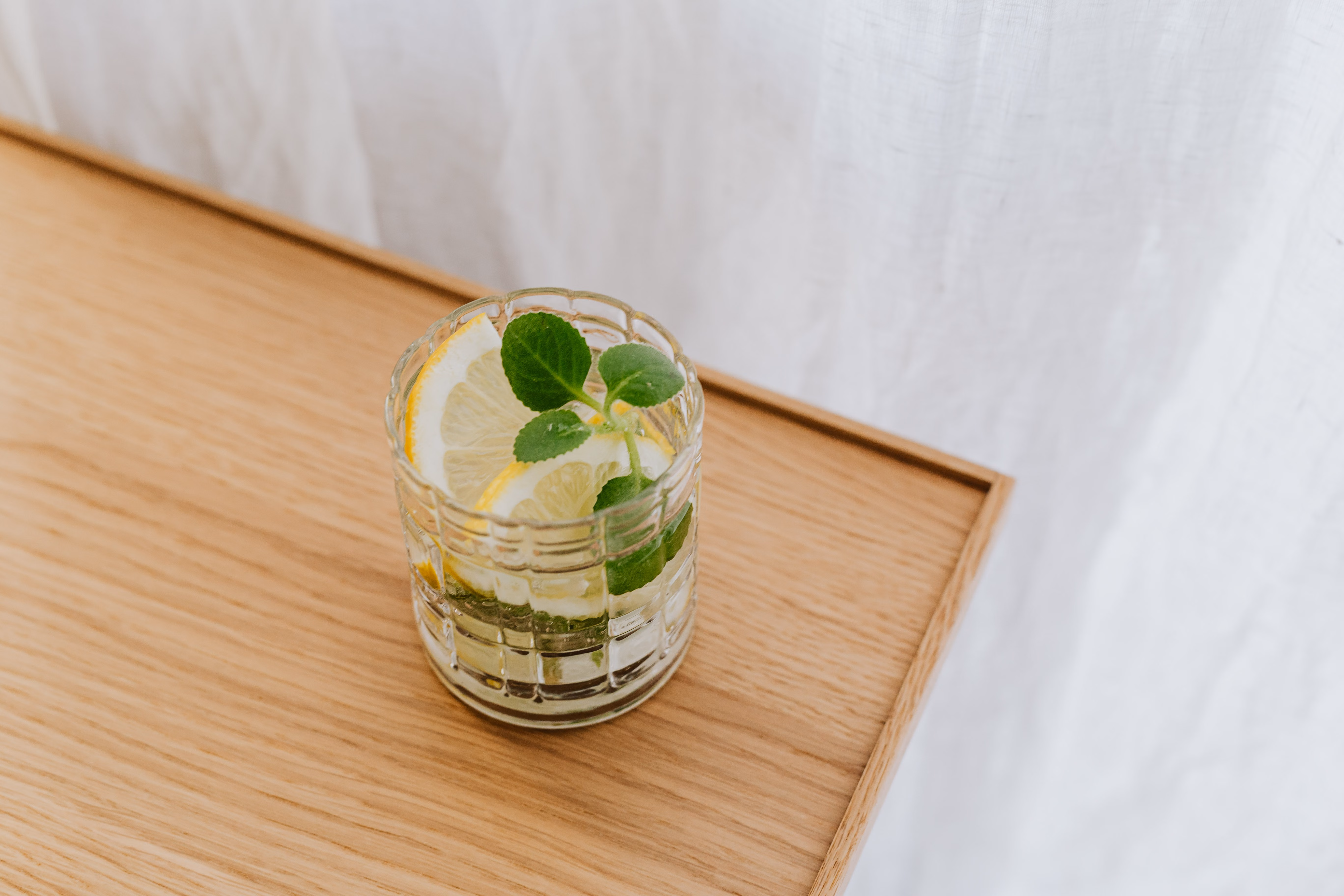 drinking enough water every day A clear glass of water on a wooden table with a lemon slice nearby